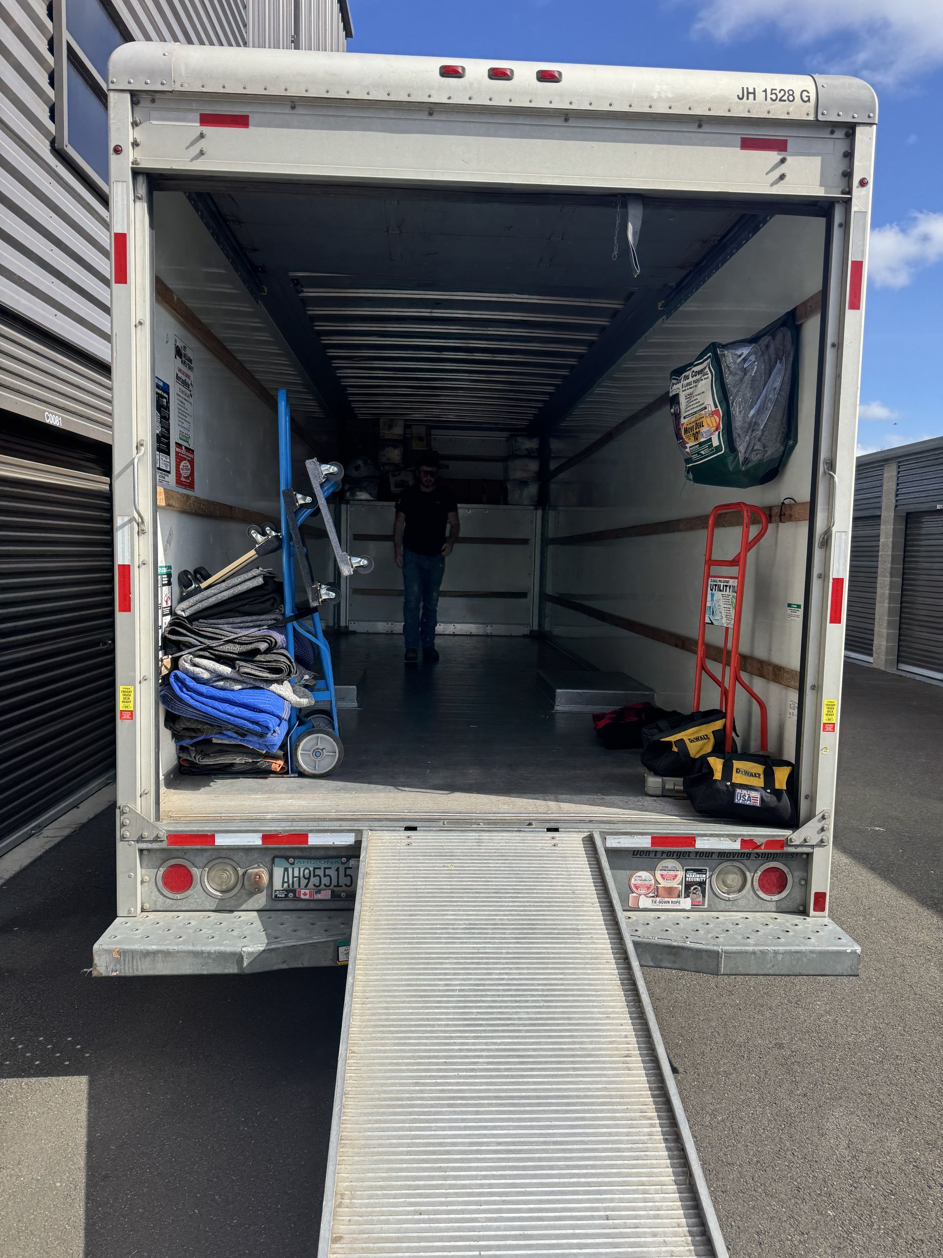 Open truck cargo area with ramp extended, ready for loading. Items visible inside: dollies, tools.