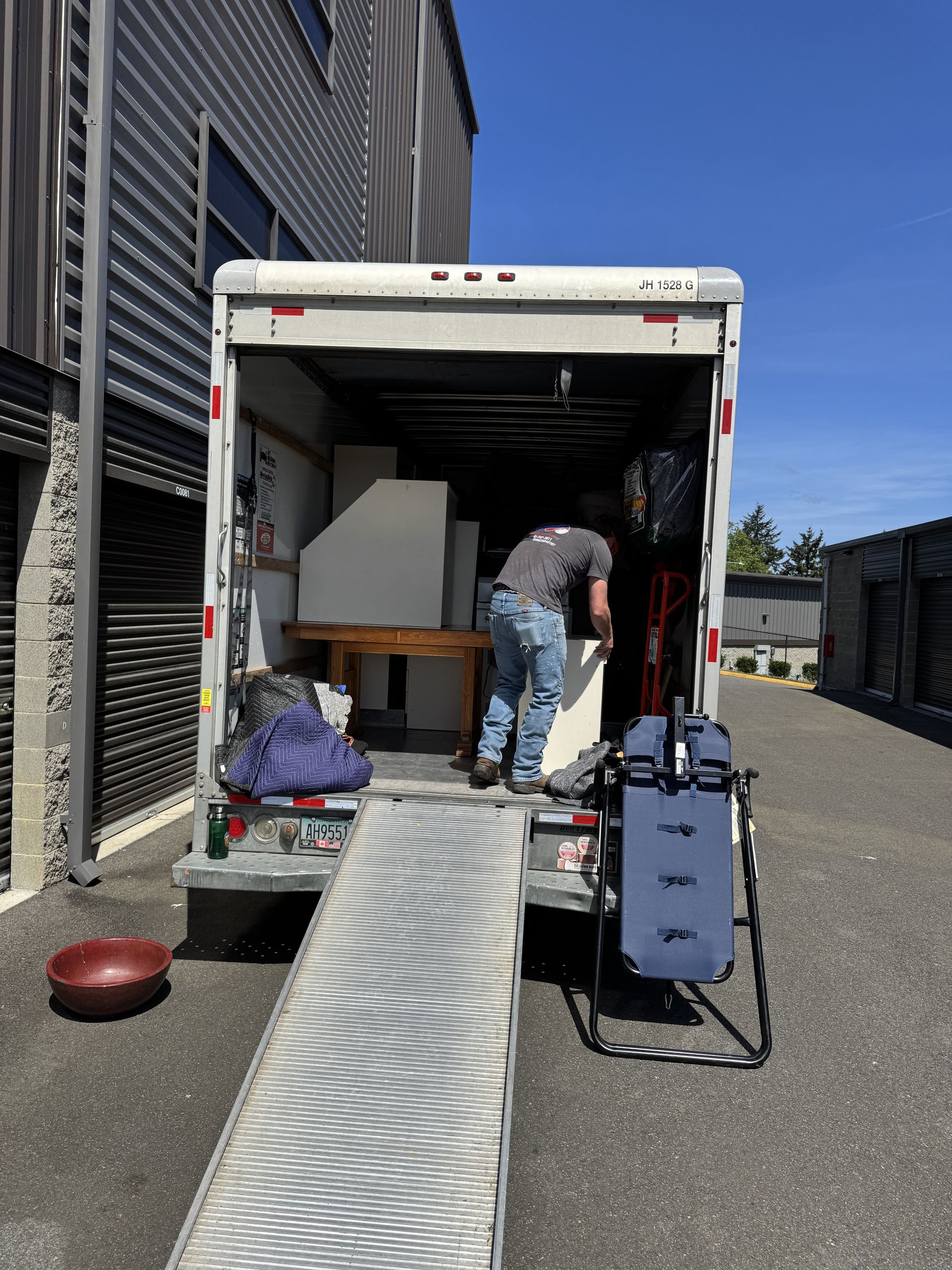 Person loading furniture into a moving truck with ramp in an outdoor setting.