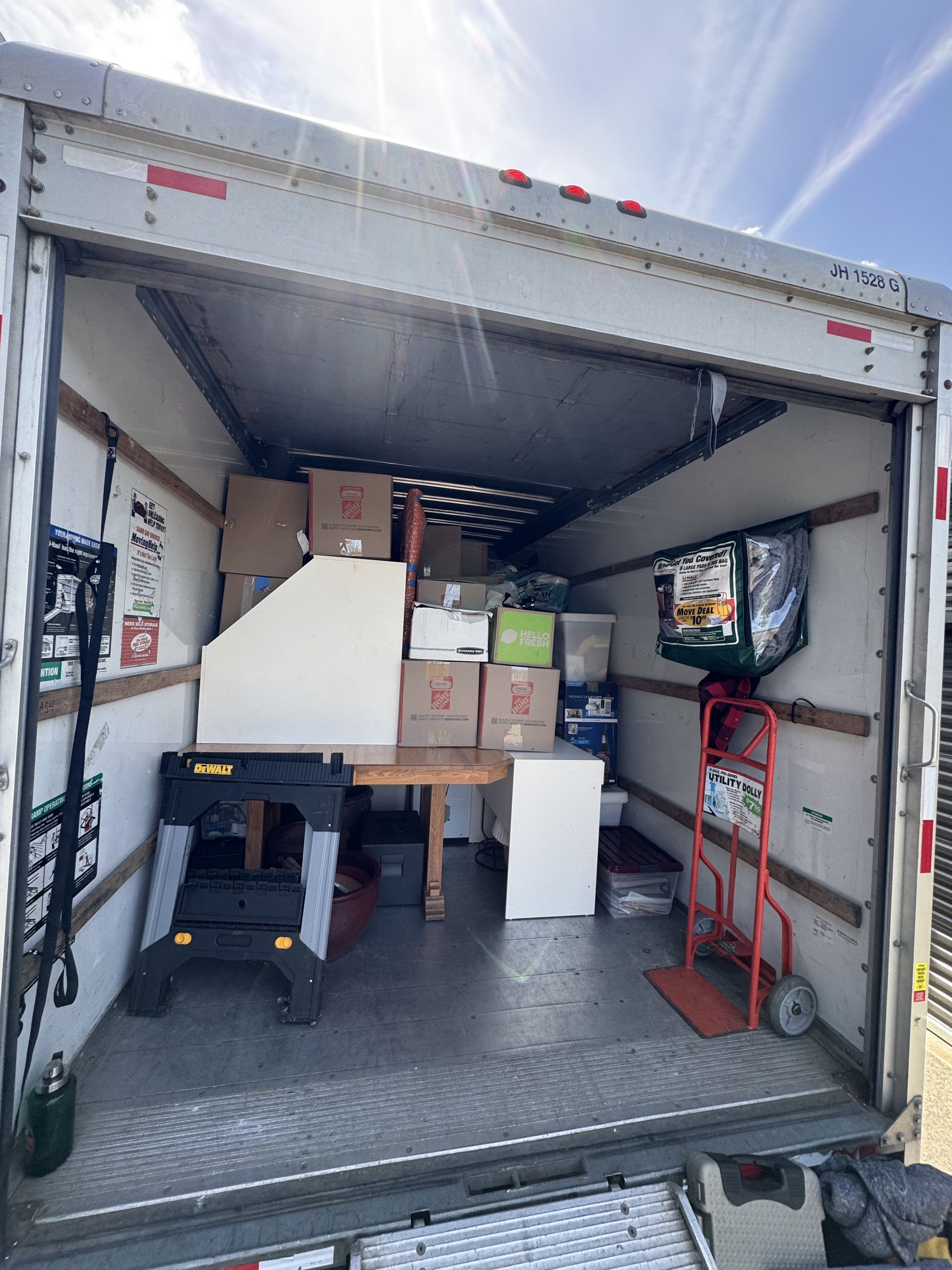 Inside a moving truck packed with boxes, a table, a work stand, and a hand truck.