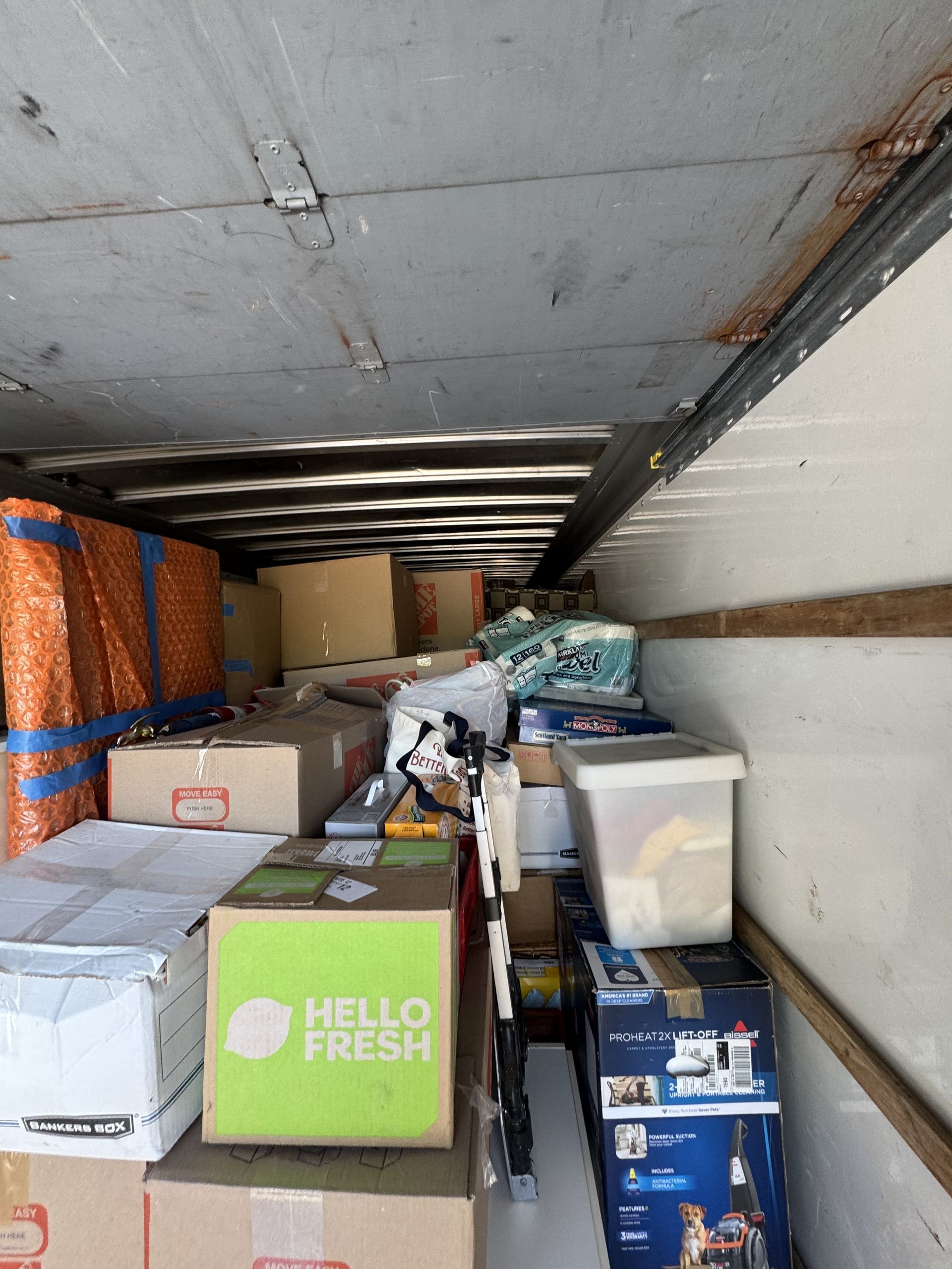 Interior of a moving truck packed with cardboard boxes and wrapped furniture, looking toward the end.