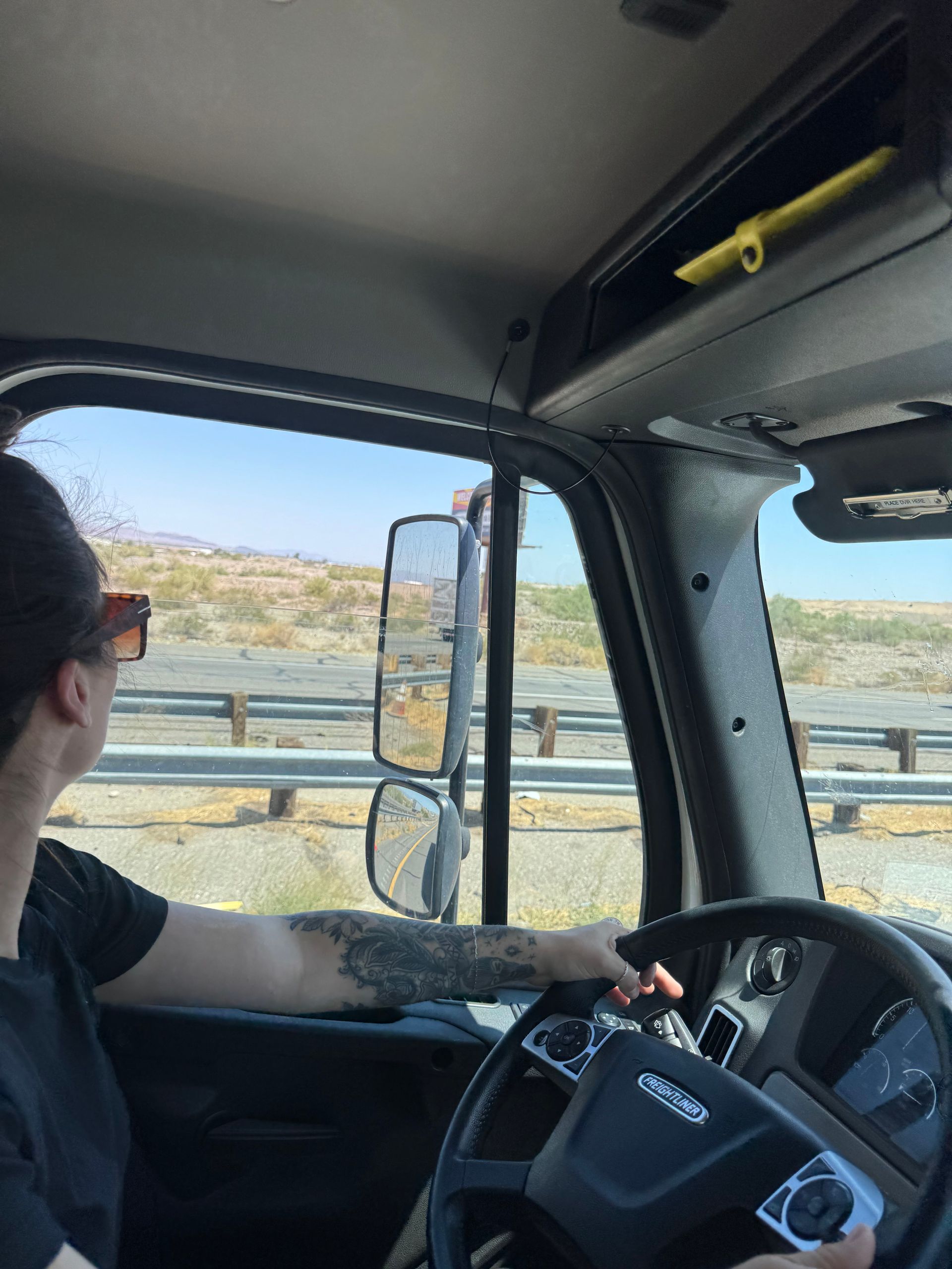 Person driving a semi-truck on a highway, desert landscape visible through the windows.