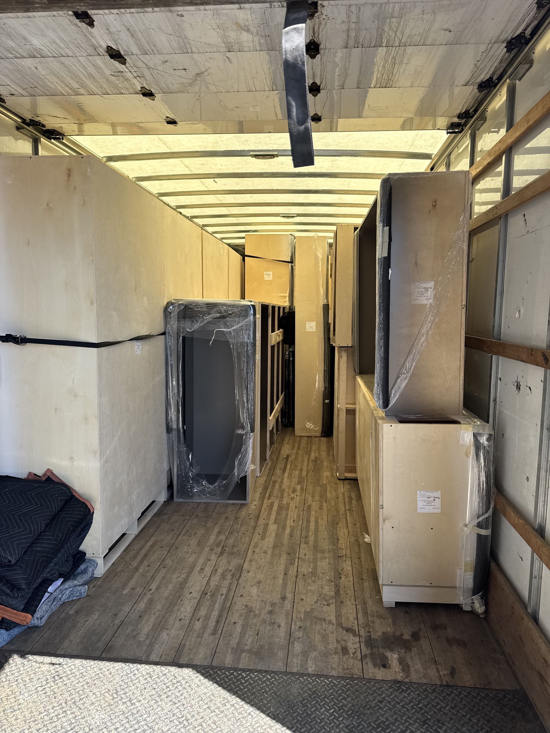 Inside a truck trailer, filled with large, wrapped boxes, appliances, and foam padding, ready for transport.