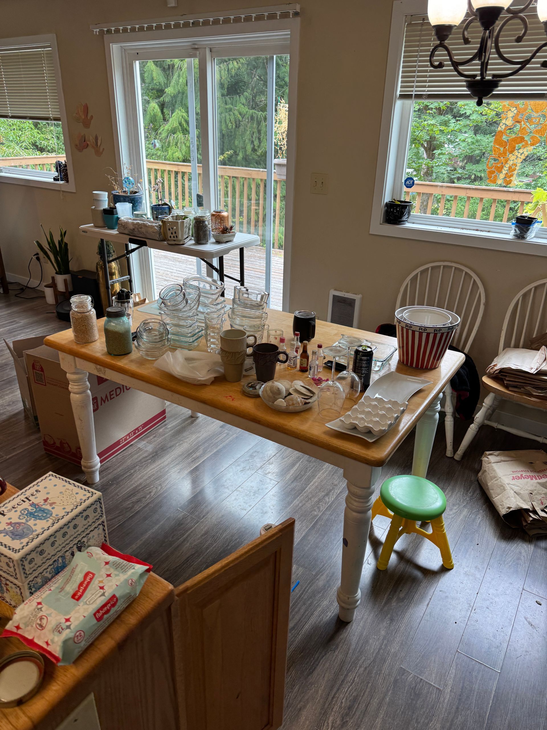 Indoor yard sale with items on tables and a view of a deck through windows.