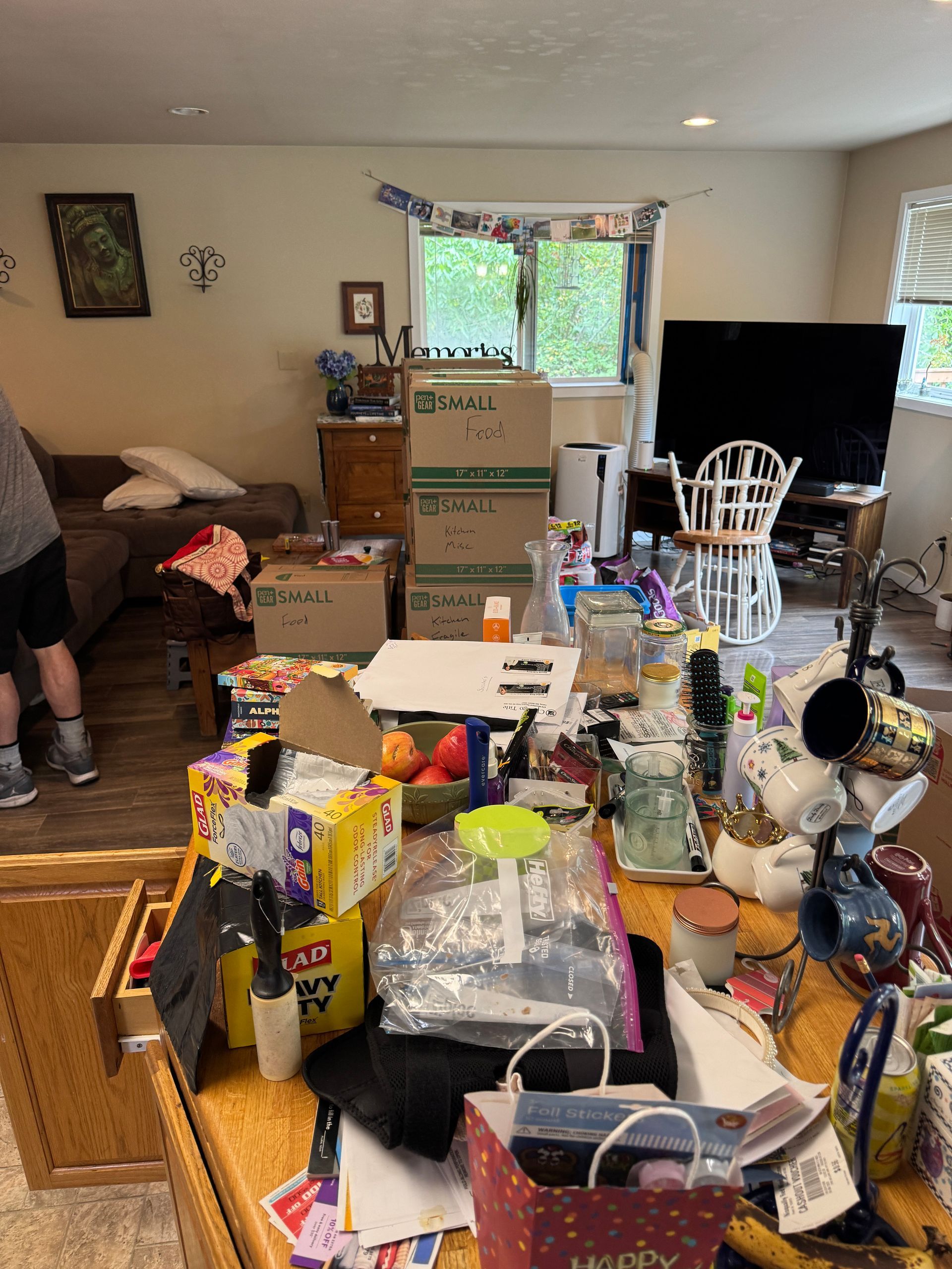 Cluttered living room with boxes, furniture, and various items on a table.