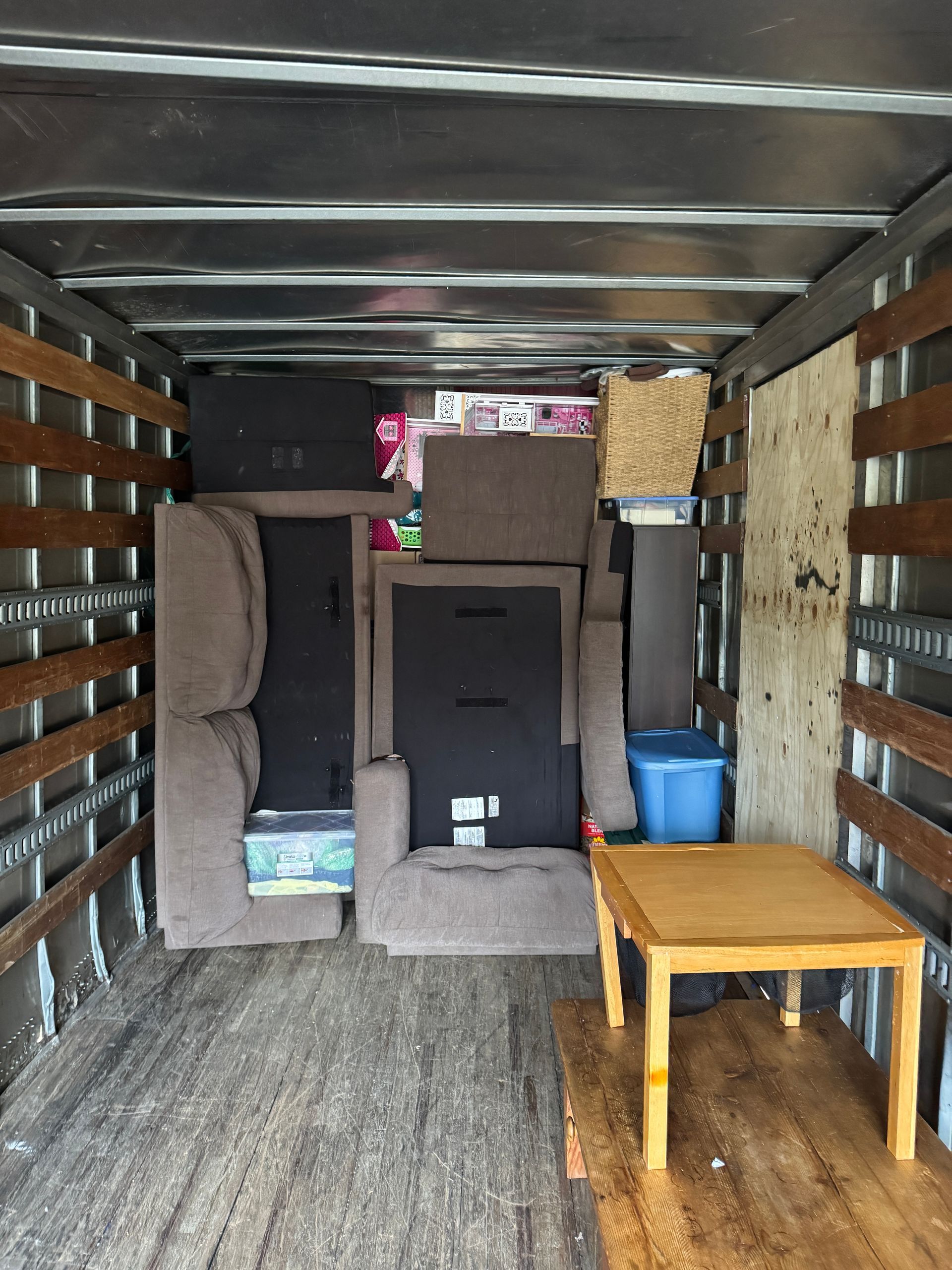 Inside of a moving truck packed with furniture and boxes, including a table and armchair.