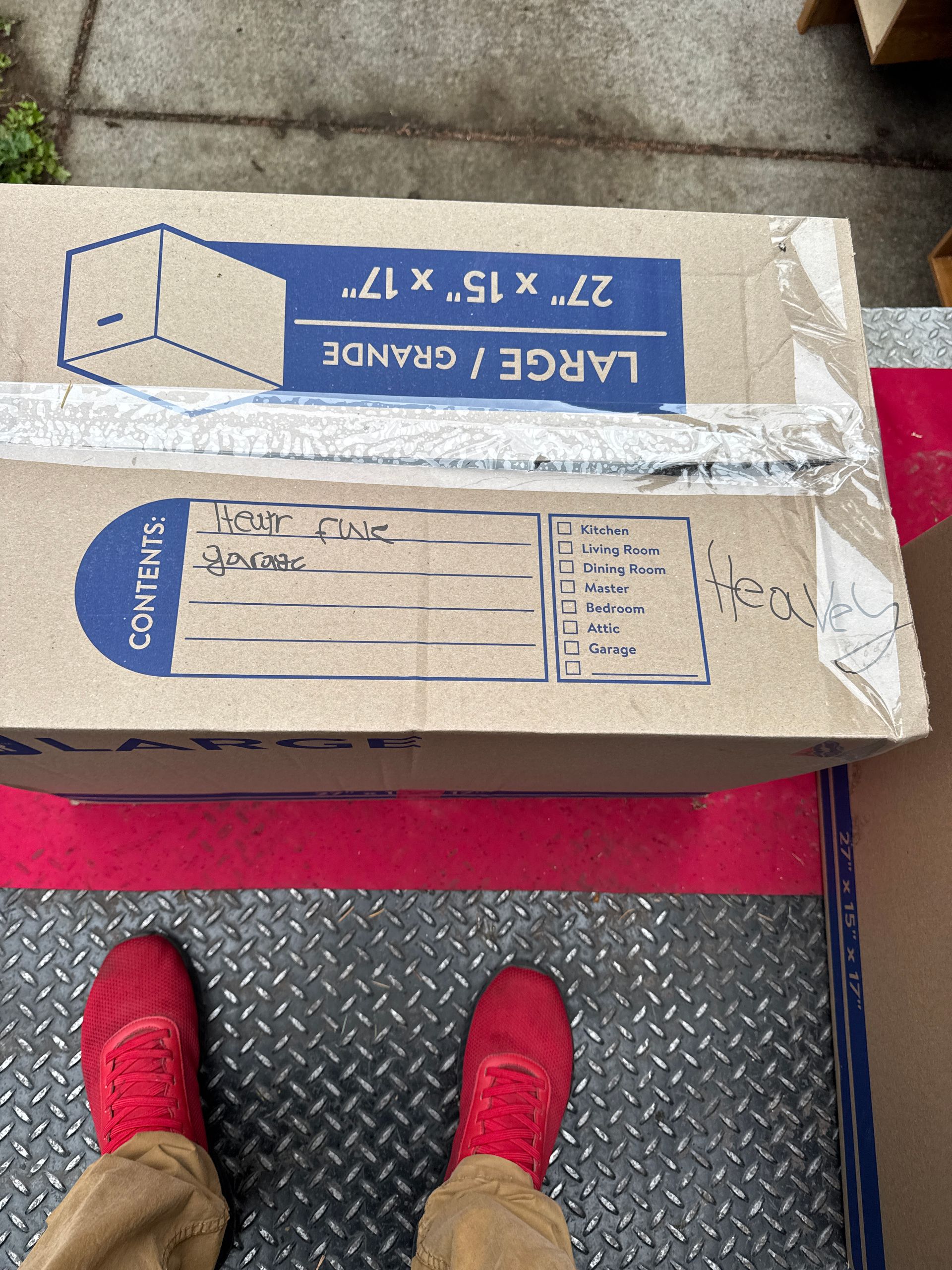 Person's feet in red shoes next to a large cardboard box labeled 