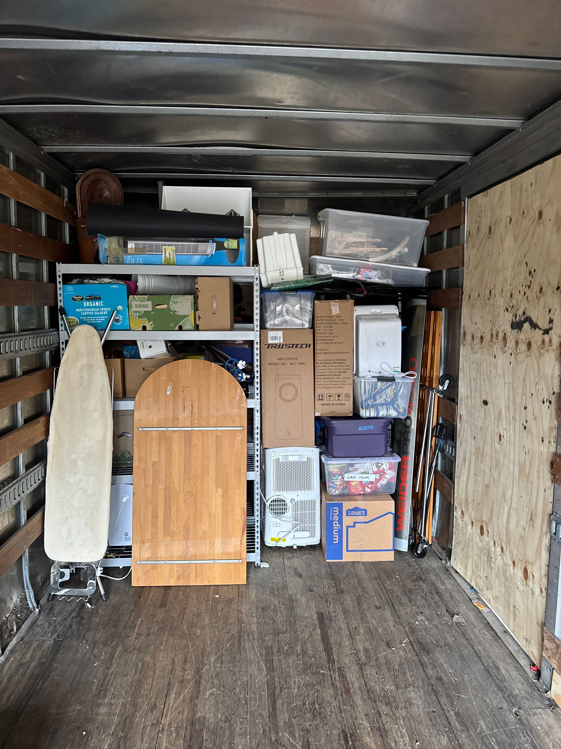 Truck interior filled with boxes, shelving, ironing board, and assorted household items.
