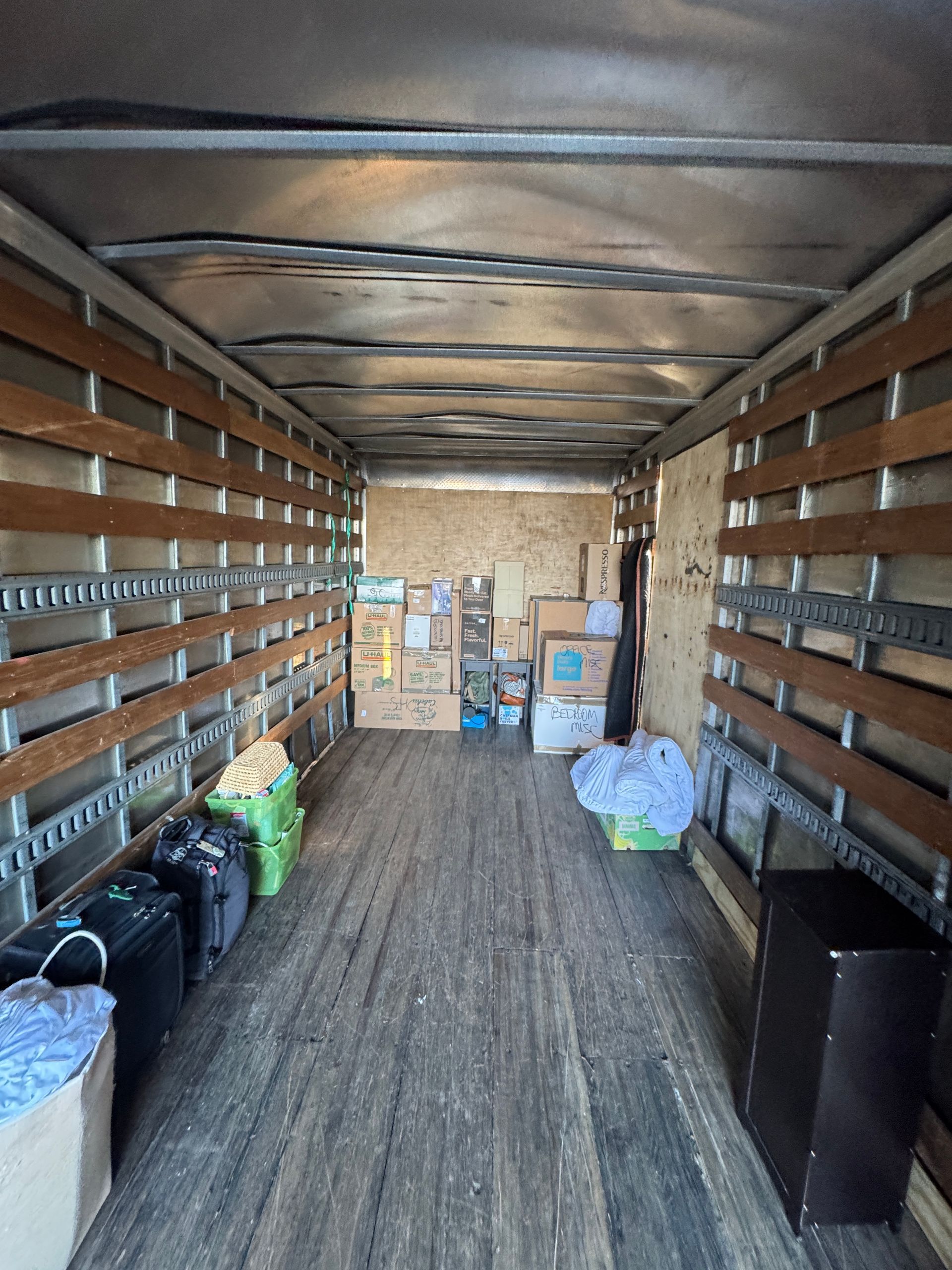 Interior of a moving truck with boxes and various items. Wooden slats line the walls.