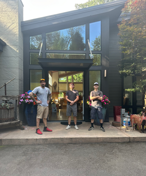 Three people standing outside a modern house, holding bouquets and gifts on the doorstep