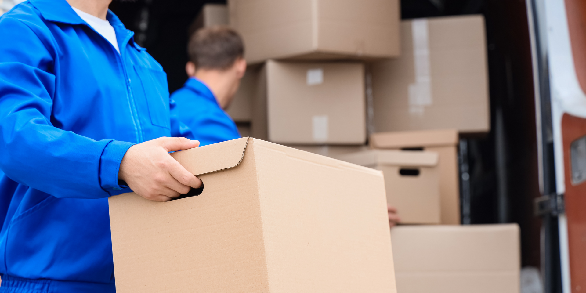 Movers unloading boxes and furniture from a truck into a two-story house on a cloudy day.