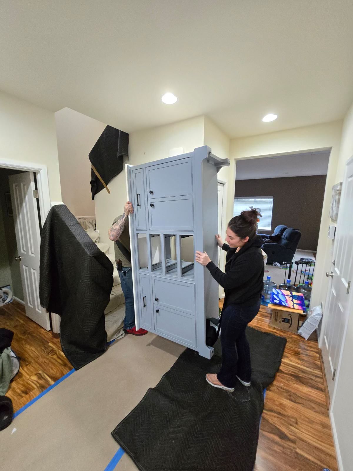Two people carrying a large gray cabinet through a doorway, hallway. One person is on a step.