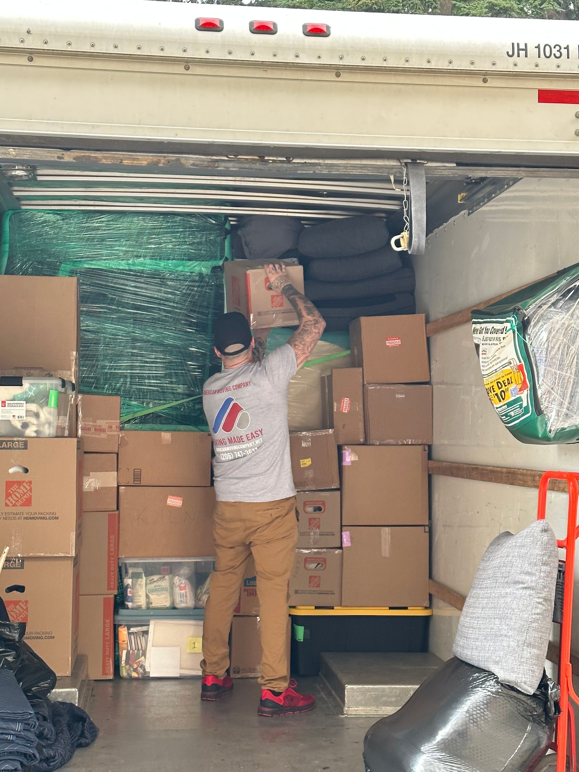 A person loading boxes into a moving truck. Boxes are stacked; various items are visible inside the truck.