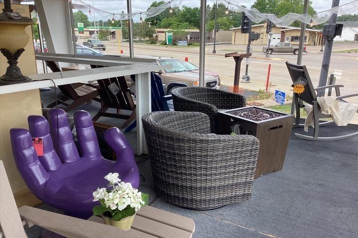 Outdoor patio furniture display, featuring a purple hand-shaped chair, wicker chairs, and a fire pit.