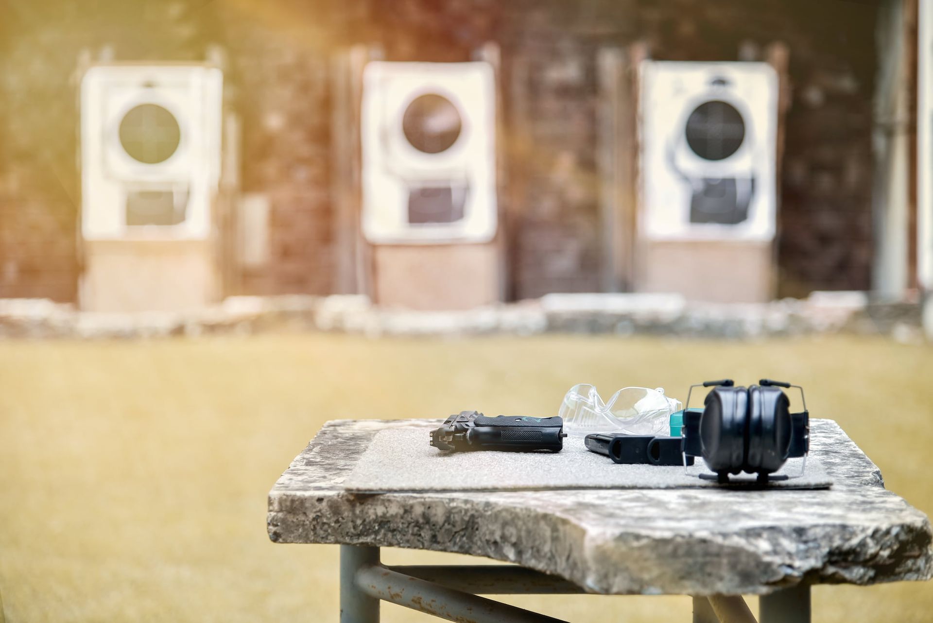 Shooting range with targets in the background, safety equipment on a table in the foreground.