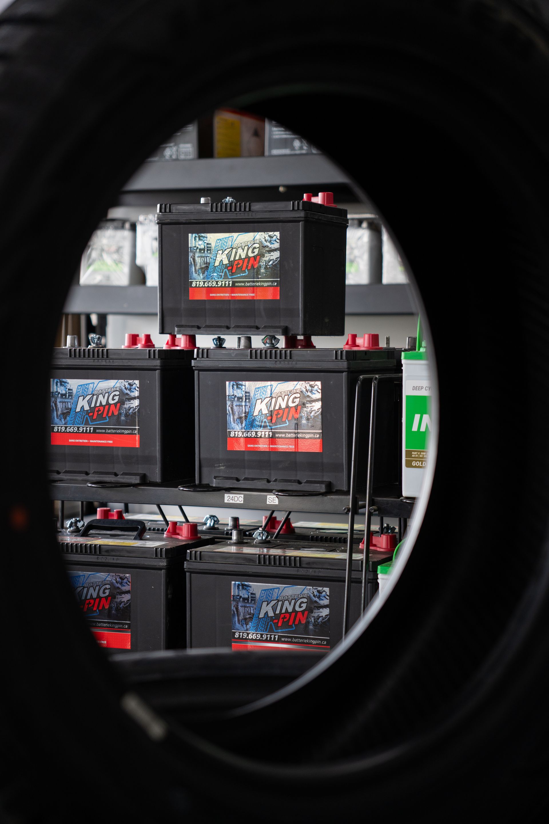 Des piles empilées sur des étagères, vues à travers le centre d'un pneu. Des piles noires avec des touches de rouge.