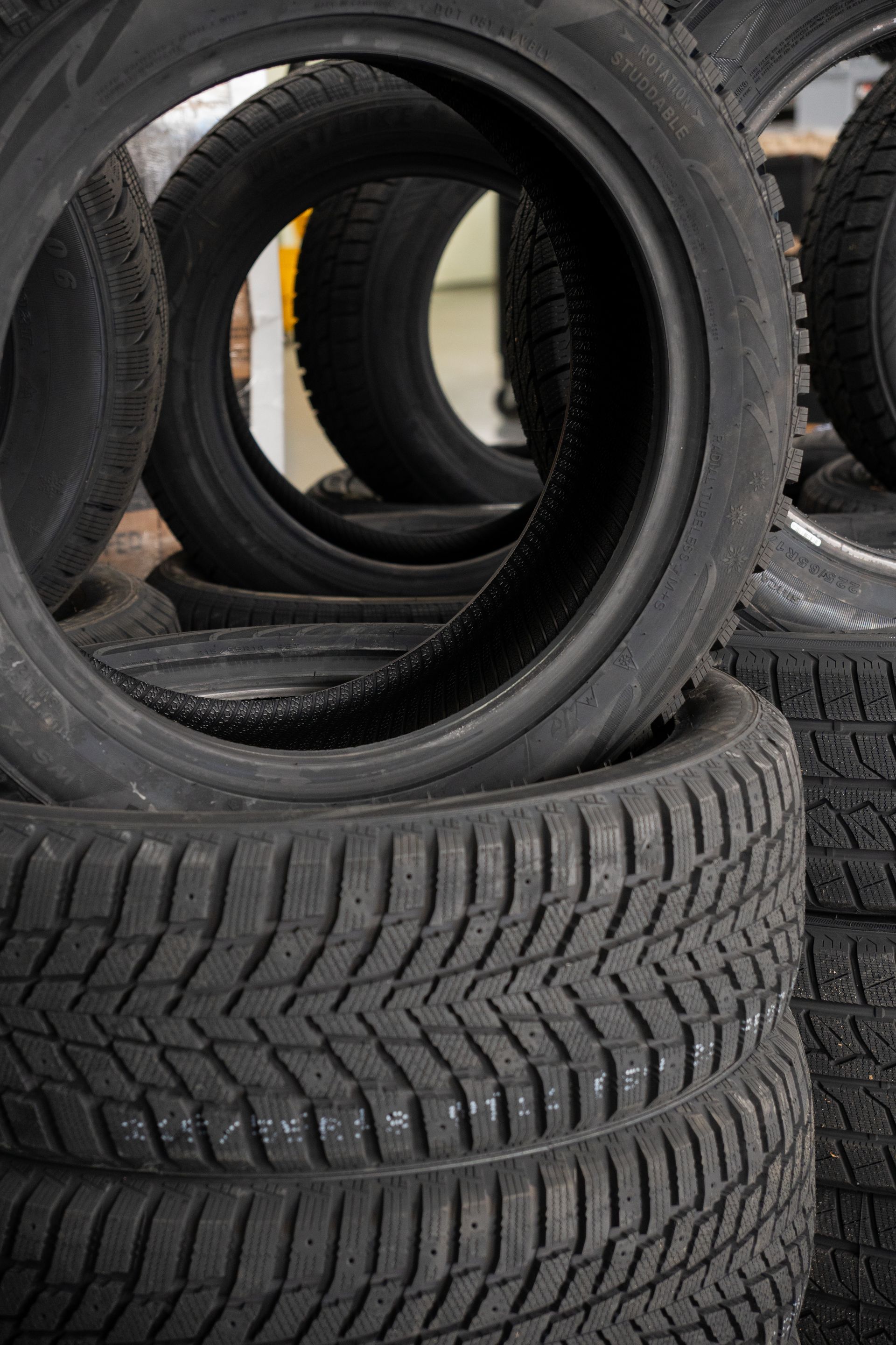 Des piles de pneus de voiture noirs, dont les sculptures sont encore visibles, dans un entrepôt.