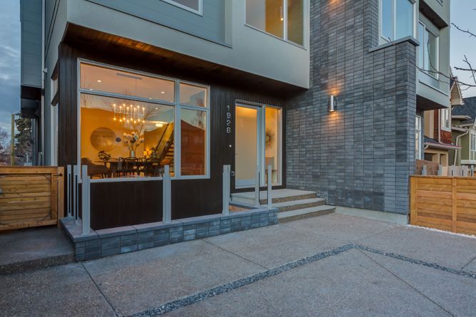 Modern townhouse entrance with a large ground-floor window, stone siding, concrete stairs, and a paved driveway.