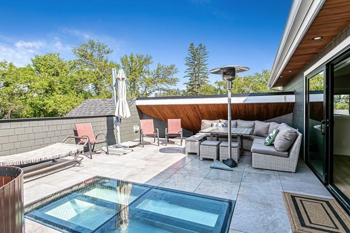 A modern outdoor rooftop terrace featuring a stone patio, lounge furniture, an umbrella, and a glass floor section.