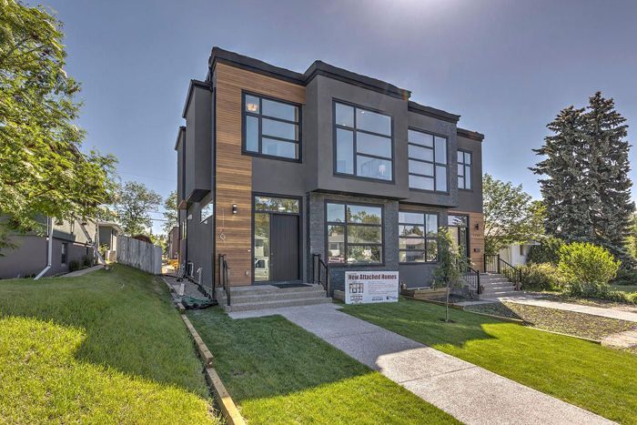 Modern, gray two-story house with black trim, large windows, and a paved walkway on a sunny day.