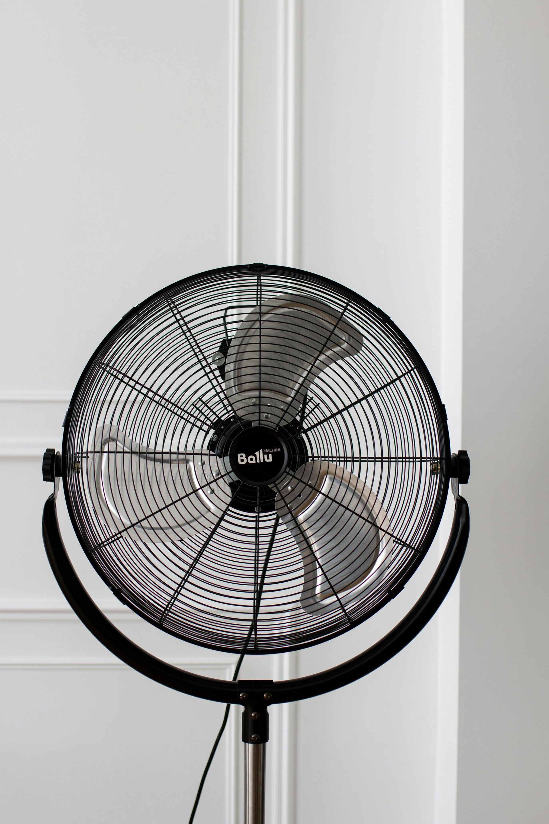 A black fan is sitting in front of a white wall.