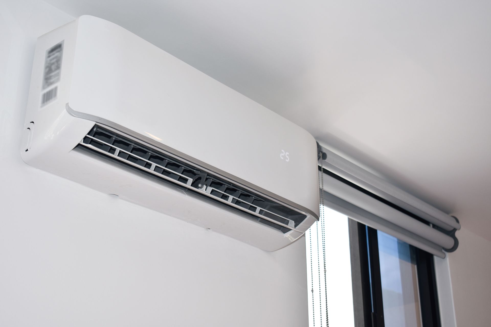 A white air conditioner is hanging from the ceiling next to a window.