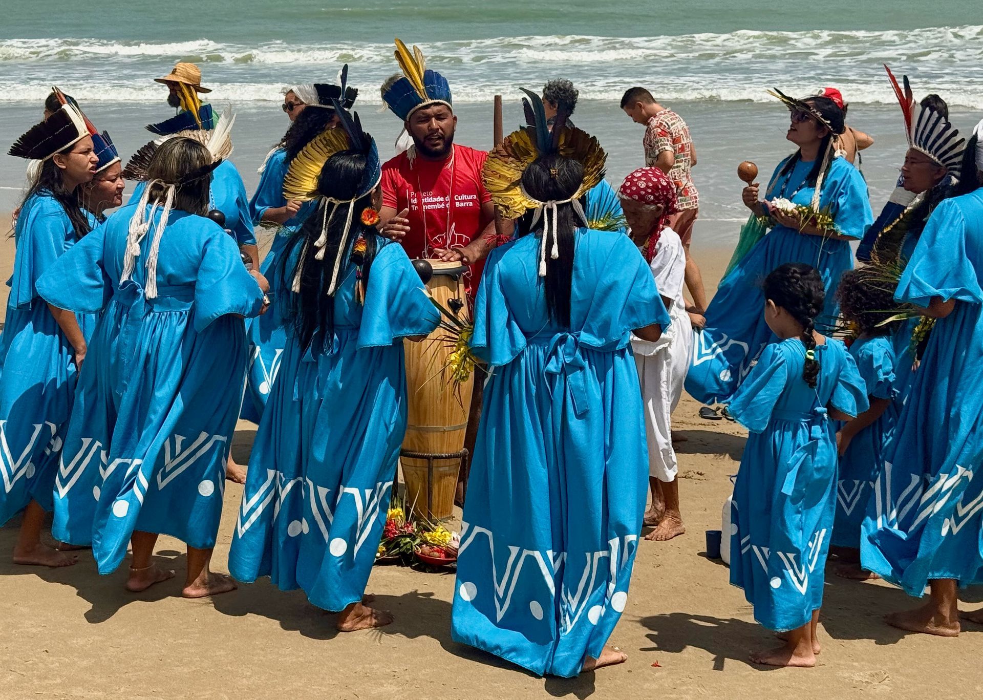 Group of people in blue robes dancing on a beach, near the ocean.