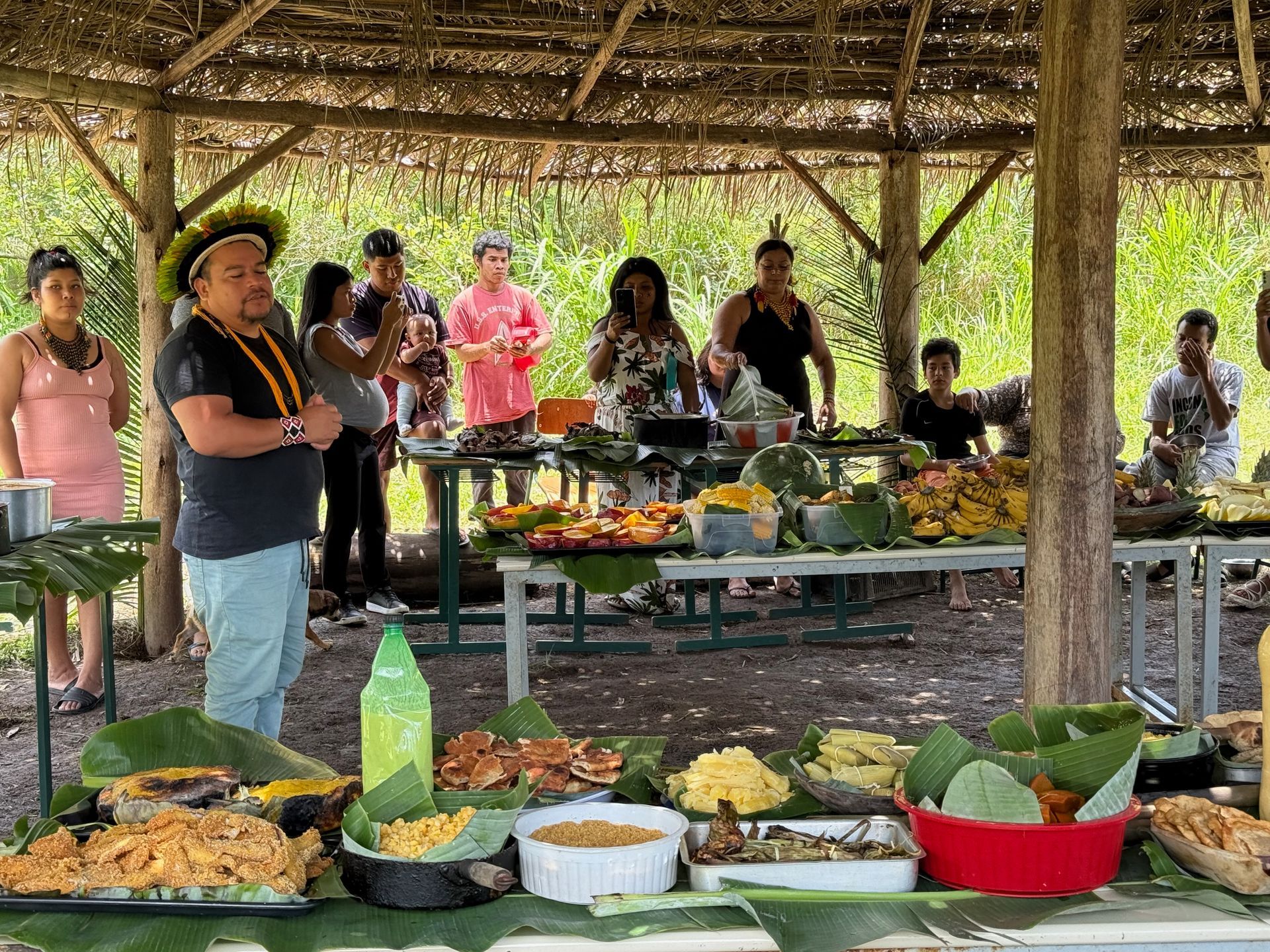 People at a food table under a wooden shelter, various dishes displayed on platters.