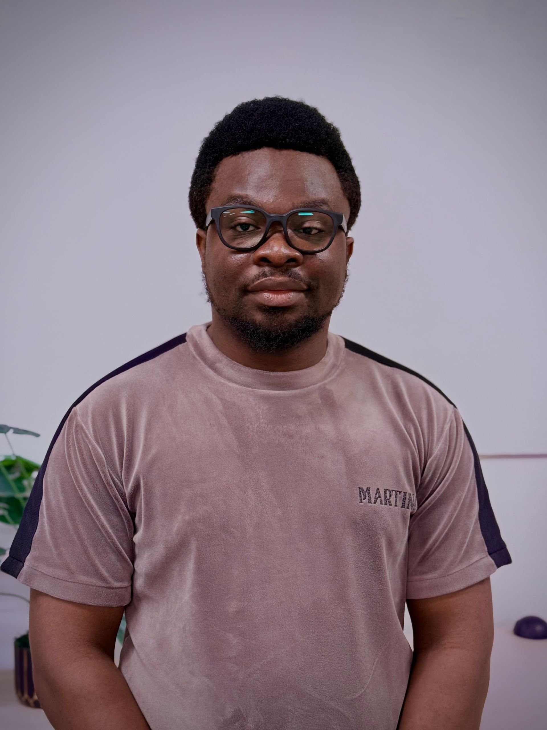Person wearing glasses and a brown shirt, looking at the camera. Neutral background.