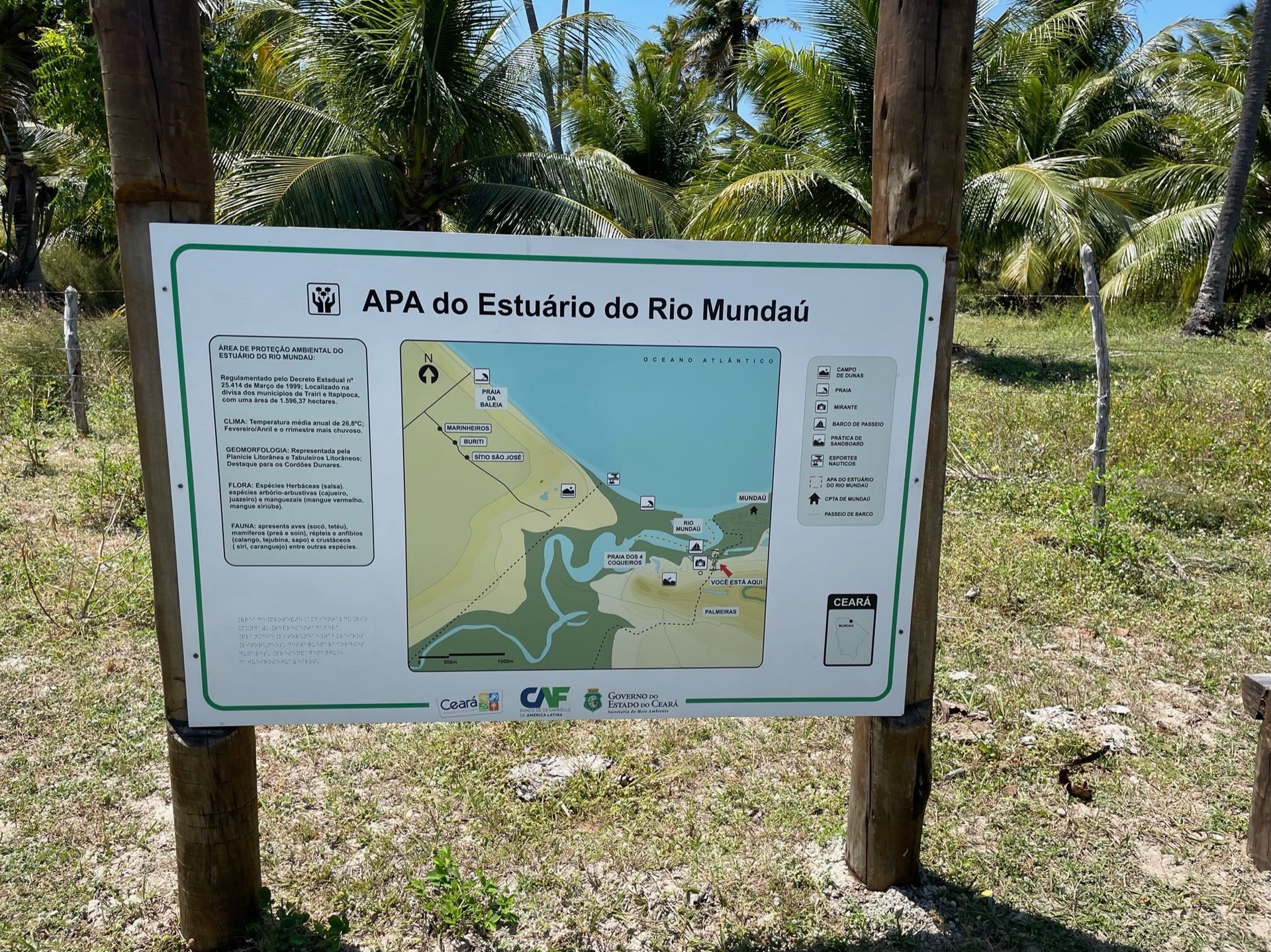 Sign with a map of a river estuary, in a grassy area with trees.