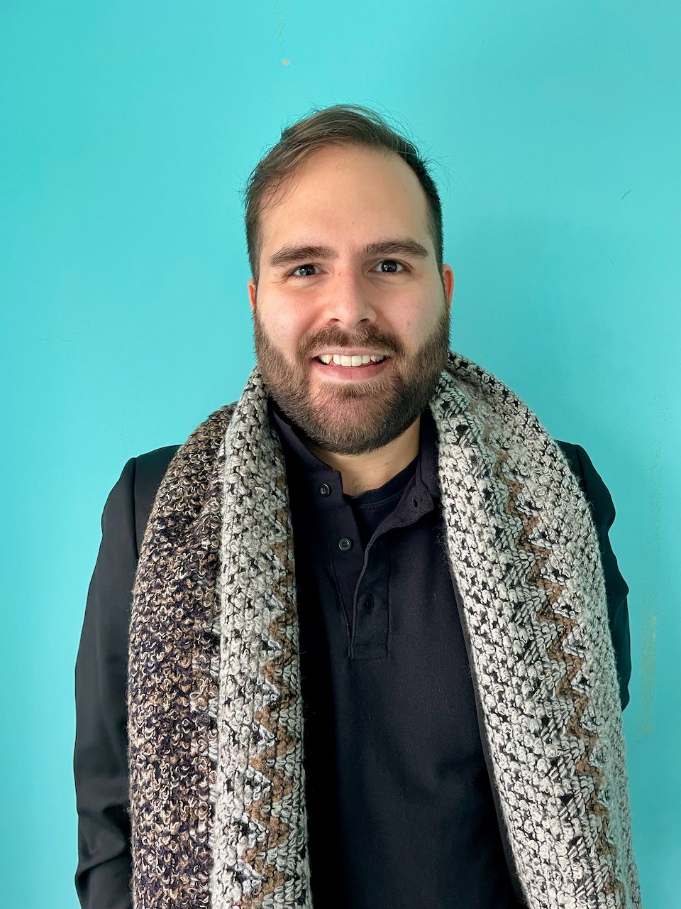 Person wearing a scarf, smiling at the camera, in front of a turquoise wall.