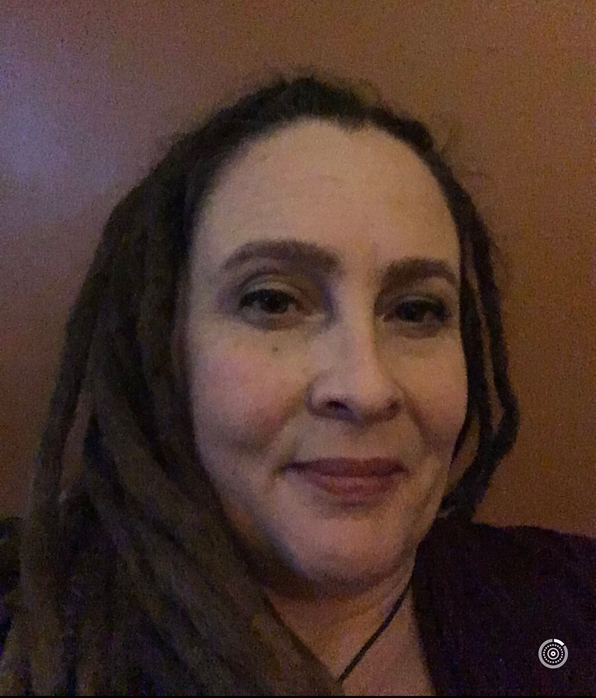 Woman with brown dreadlocks smiles, looking at the viewer. Blurred background is brown.