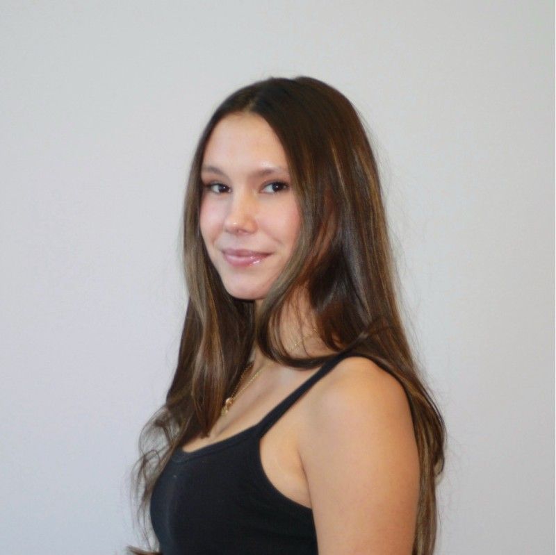 Person with long brown hair, wearing a black tank top, smiling, against a white background.