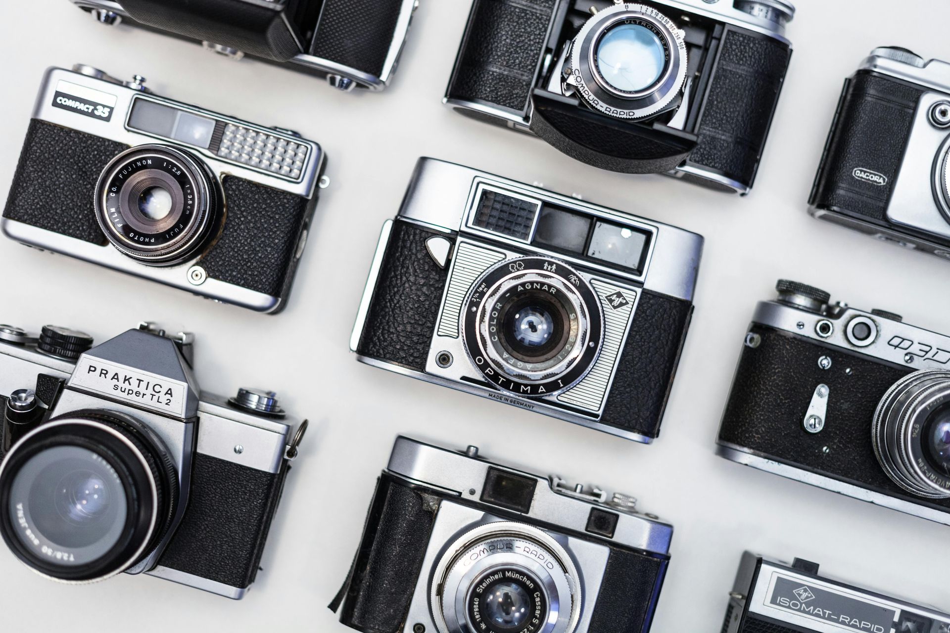 Assortment of vintage cameras with silver and black bodies, arranged on a white surface.