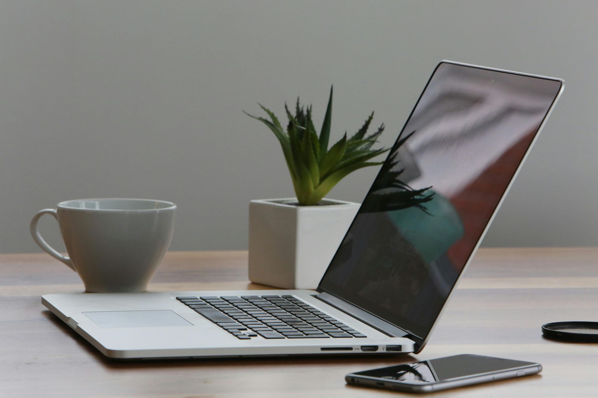 Laptop, mug, plant, and smartphone on a wooden desk.