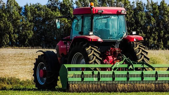 A red tractor is driving through a grassy field