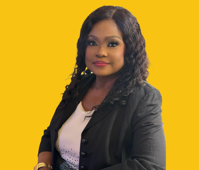 Woman in a black blazer and white top smiles at the camera against a yellow backdrop.