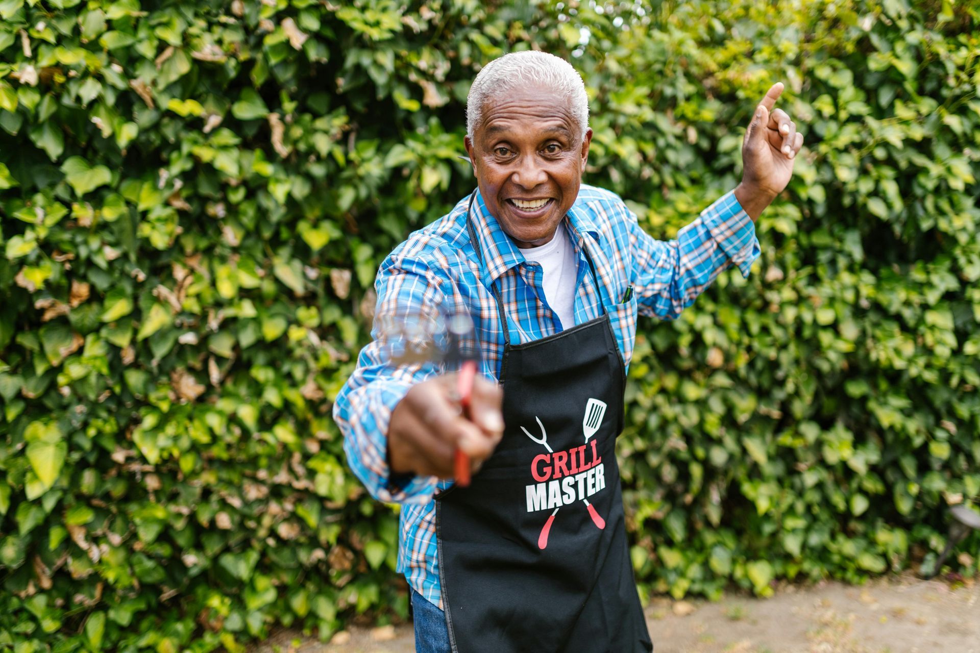 Smiling senior man grilling, pointing, wearing