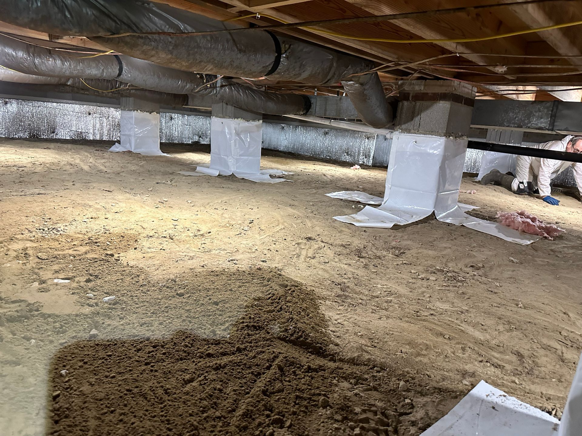 A man is working underneath a house with a lot of pipes.