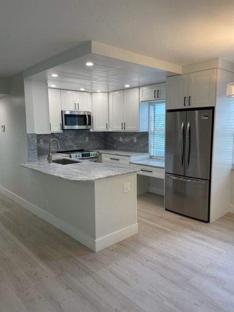 A kitchen with white cabinets and a stainless steel refrigerator