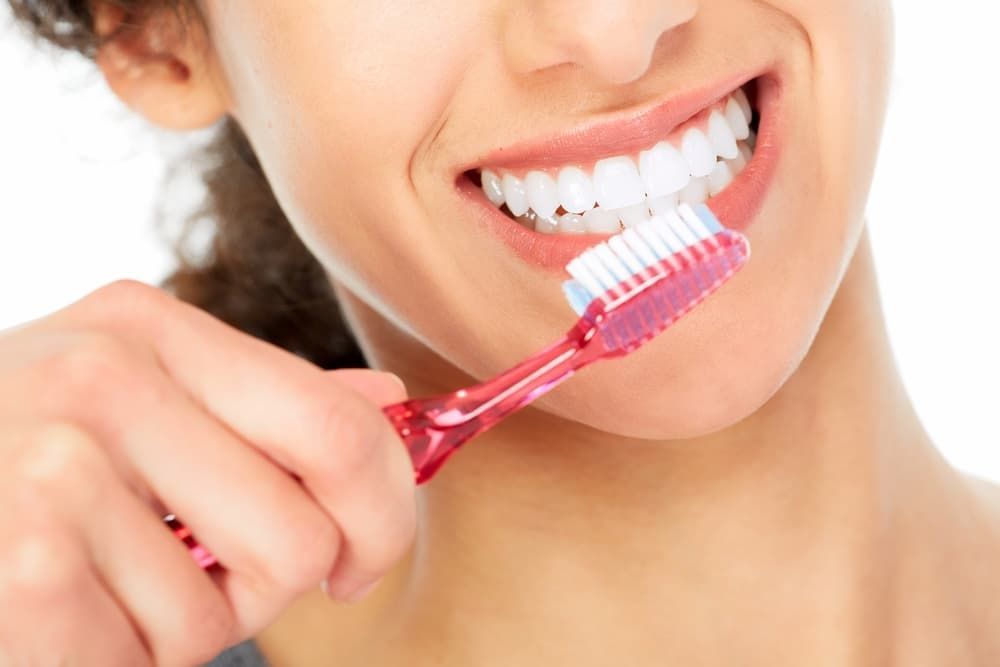 A Person Smiling While Brushing Their Teeth With a Red Toothbrush