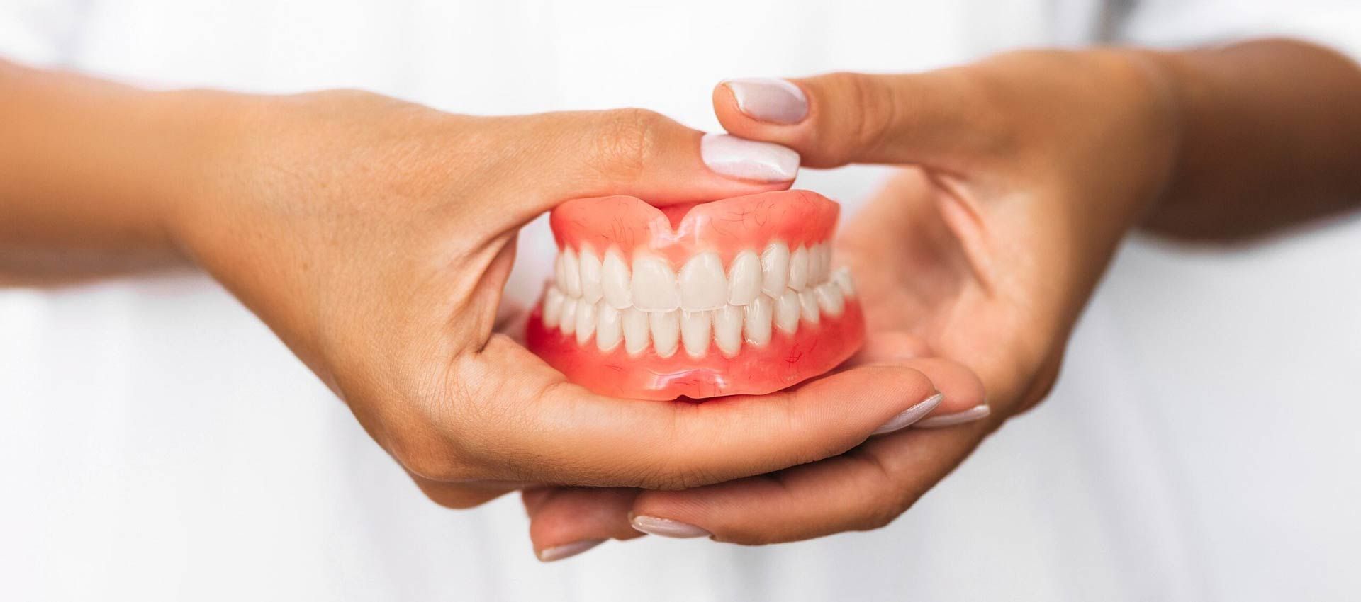 A Woman Is Holding A Denture In Her Hands — St Ives Dental Boutique In Saint Ives, NSW