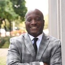 A man in a suit and tie is smiling with his arms crossed.