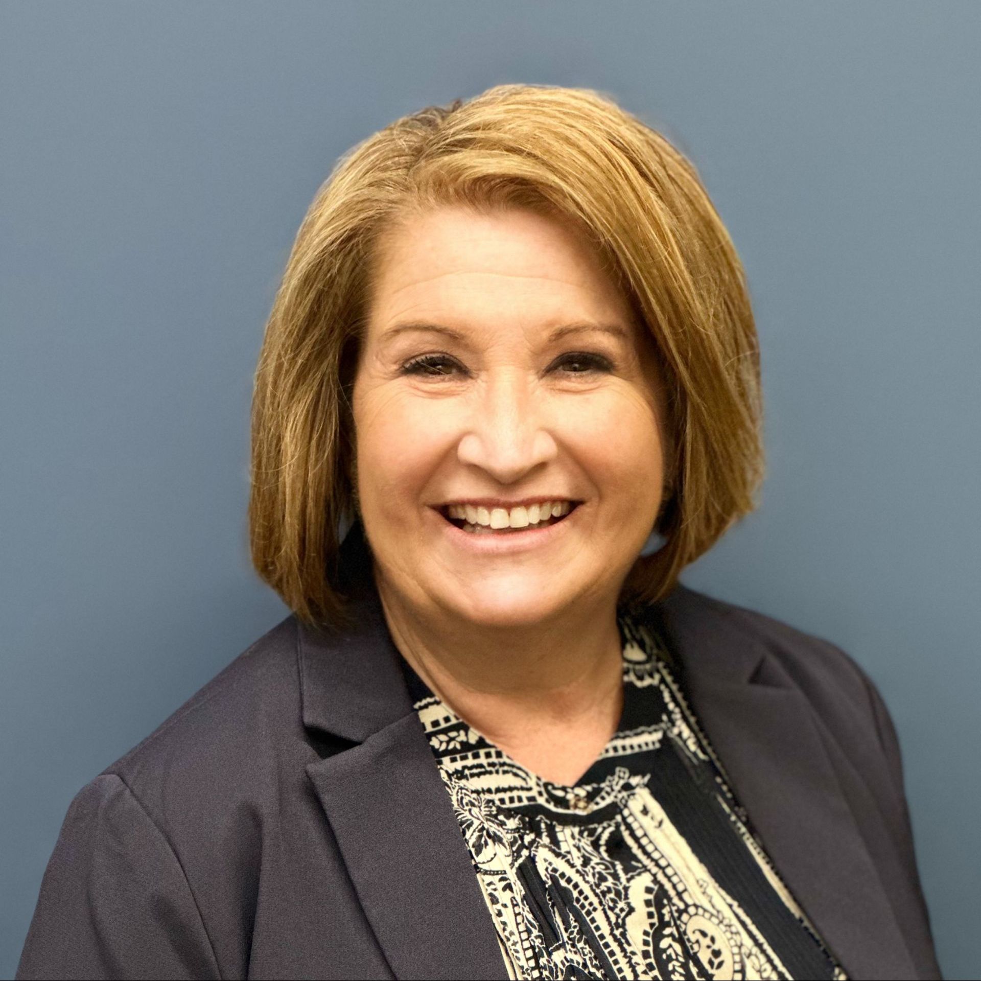 A woman wearing a jacket and a striped shirt is smiling for the camera.