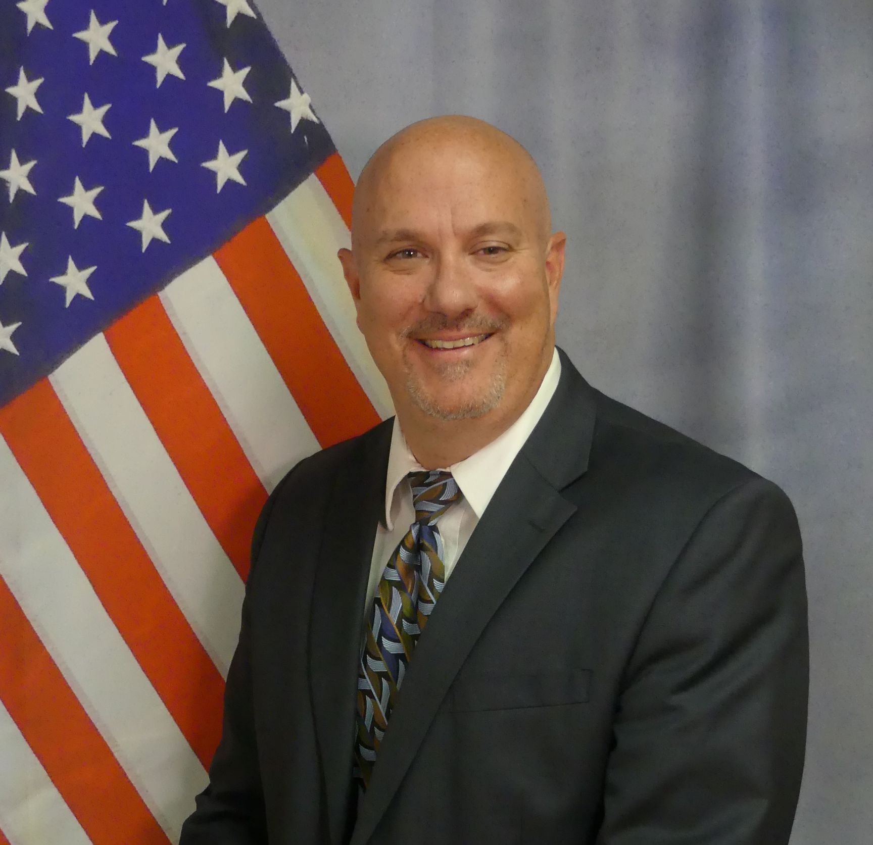 A man in a suit and tie is smiling in front of an american flag