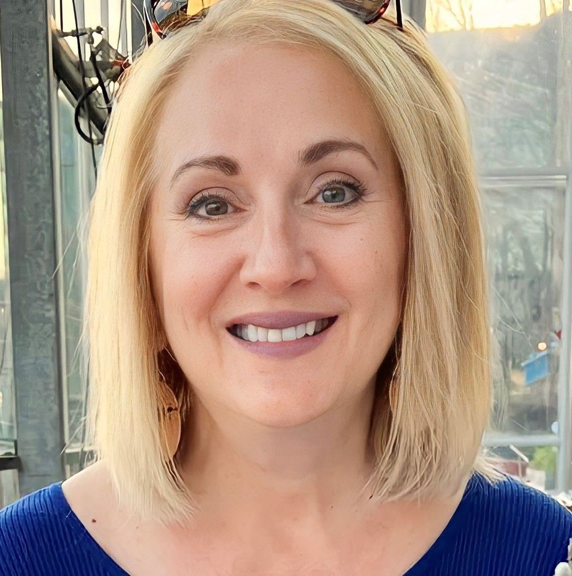 A woman wearing sunglasses and a blue shirt is smiling for the camera.