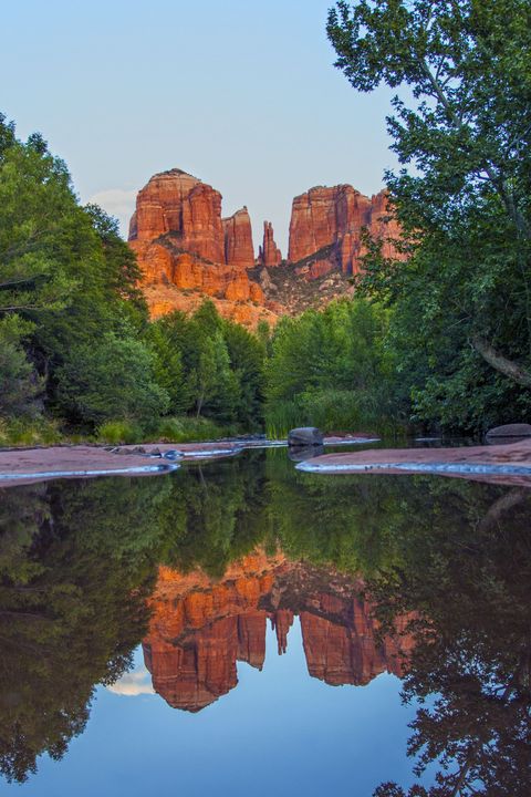 A river surrounded by trees and rocks with a reflection of a mountain in the water.