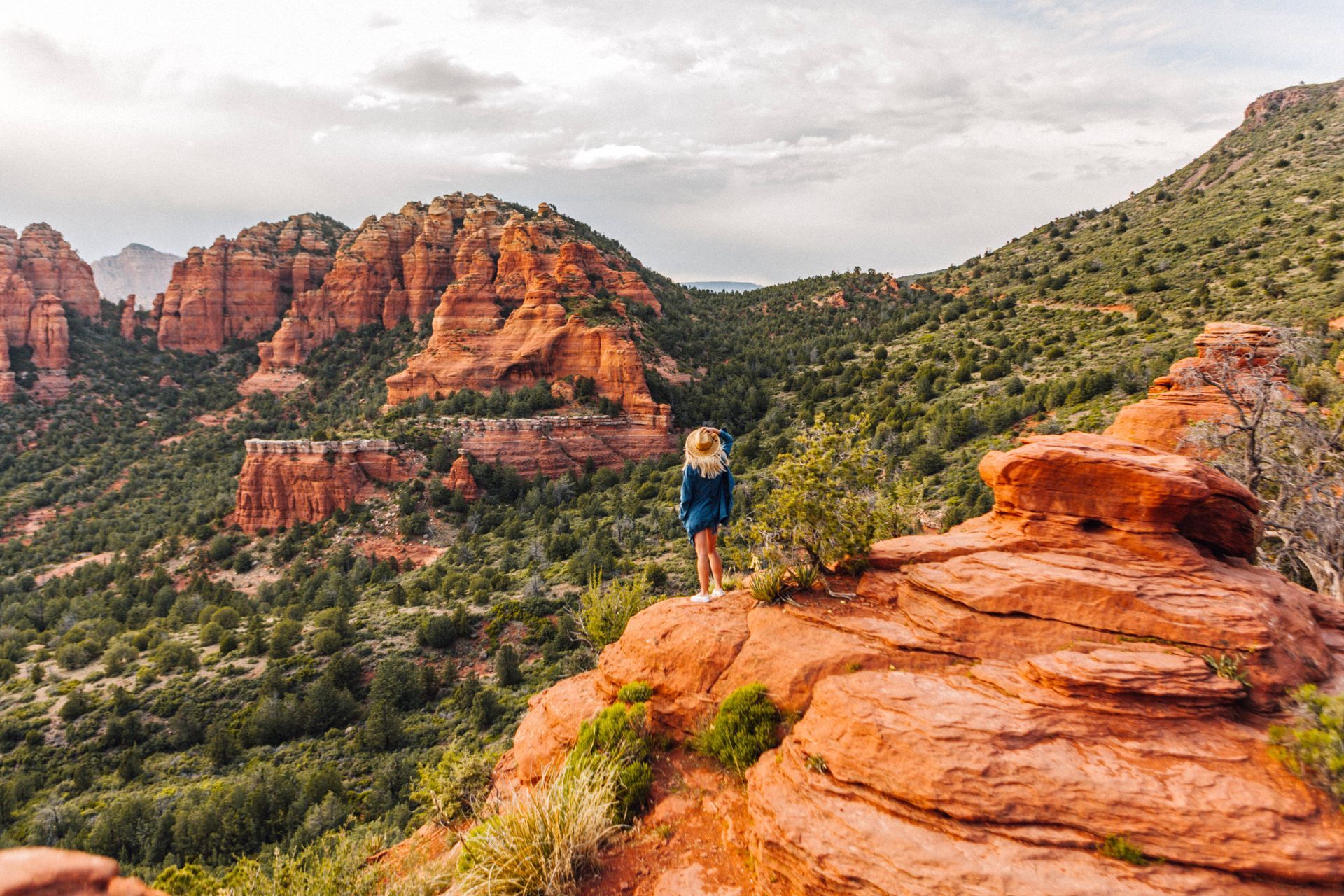 A woman is standing on top of a rocky cliff overlooking a valley.