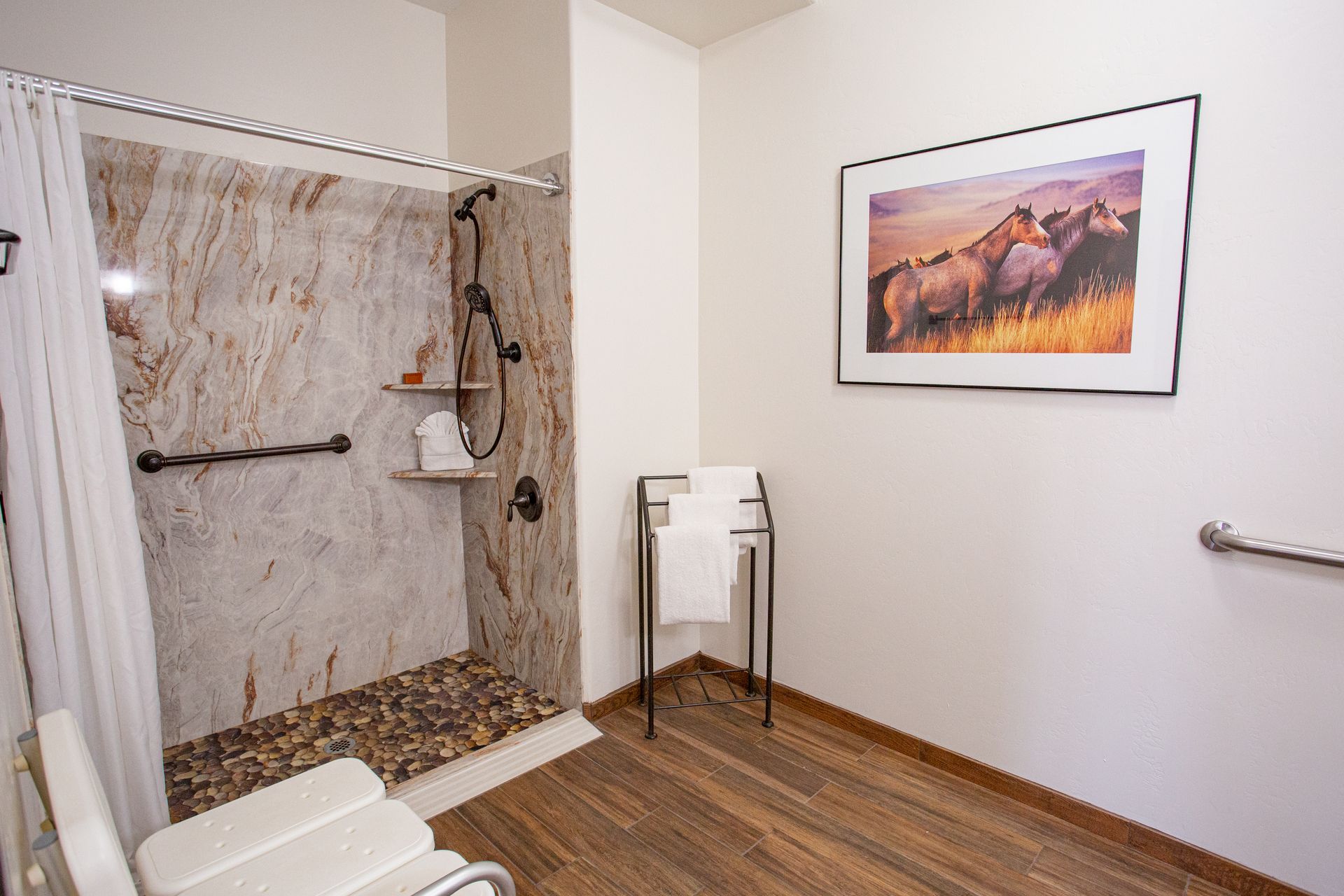 A bathroom with a walk in shower and a picture of horses on the wall.