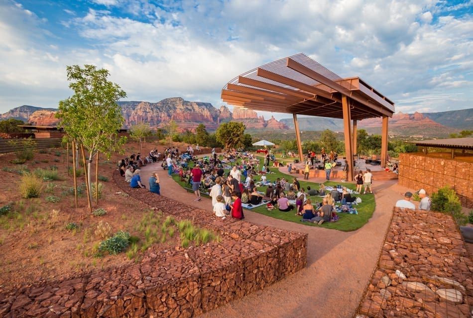 A large group of people are sitting under a covered amphitheater in the desert.