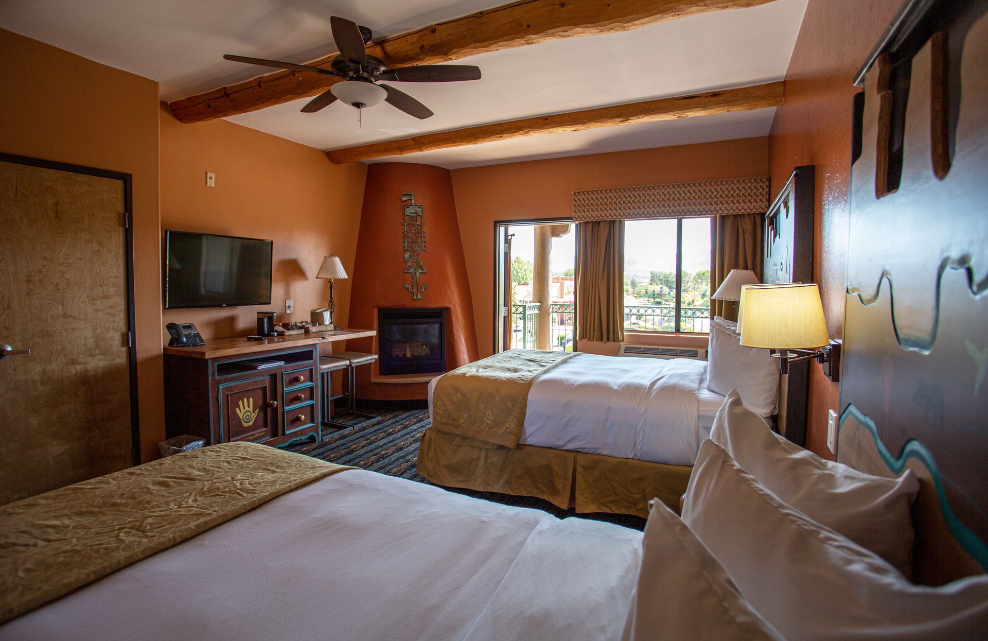 A hotel room with two beds , a fireplace , a flat screen tv and a ceiling fan.